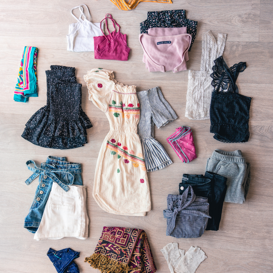 Five sorted piles of children's clothing on a bed during a wardrobe sort